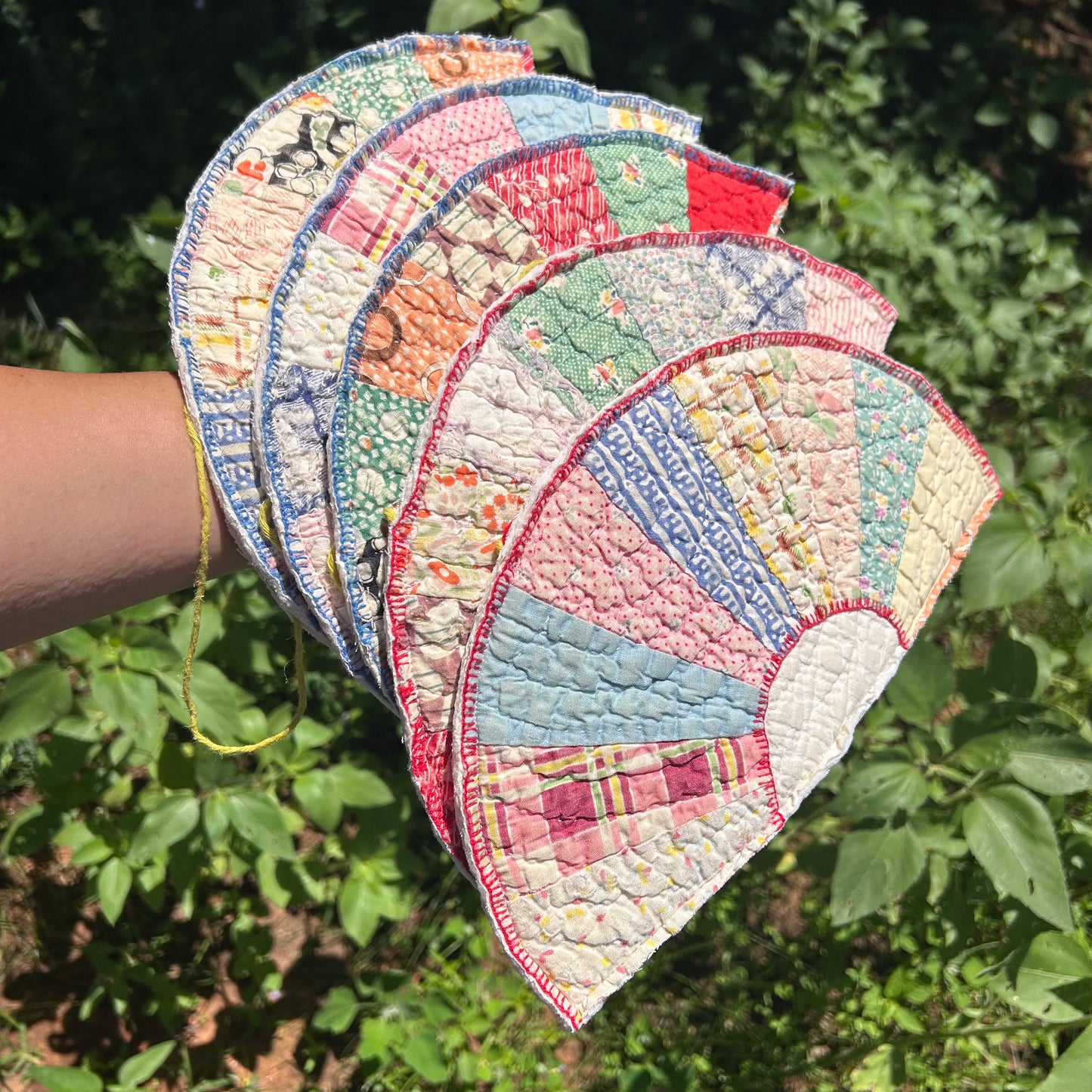Stack of colorful quilted coasters held against a green leafy background