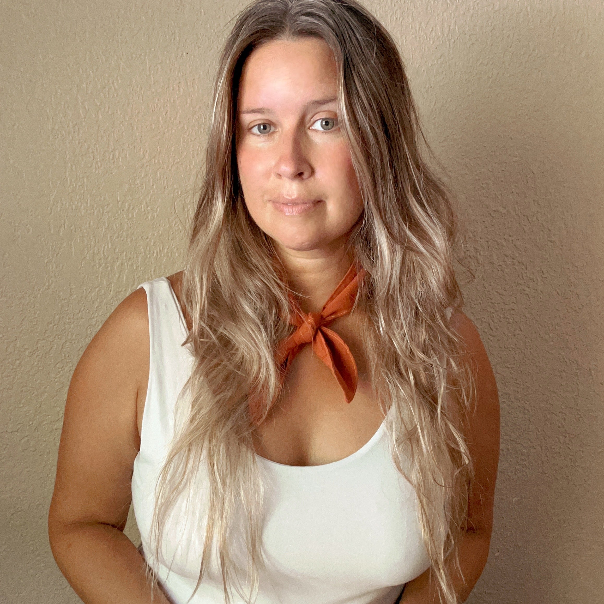 a photo of a woman with long hair and a white tank top and an orange neck scarf with a beige background