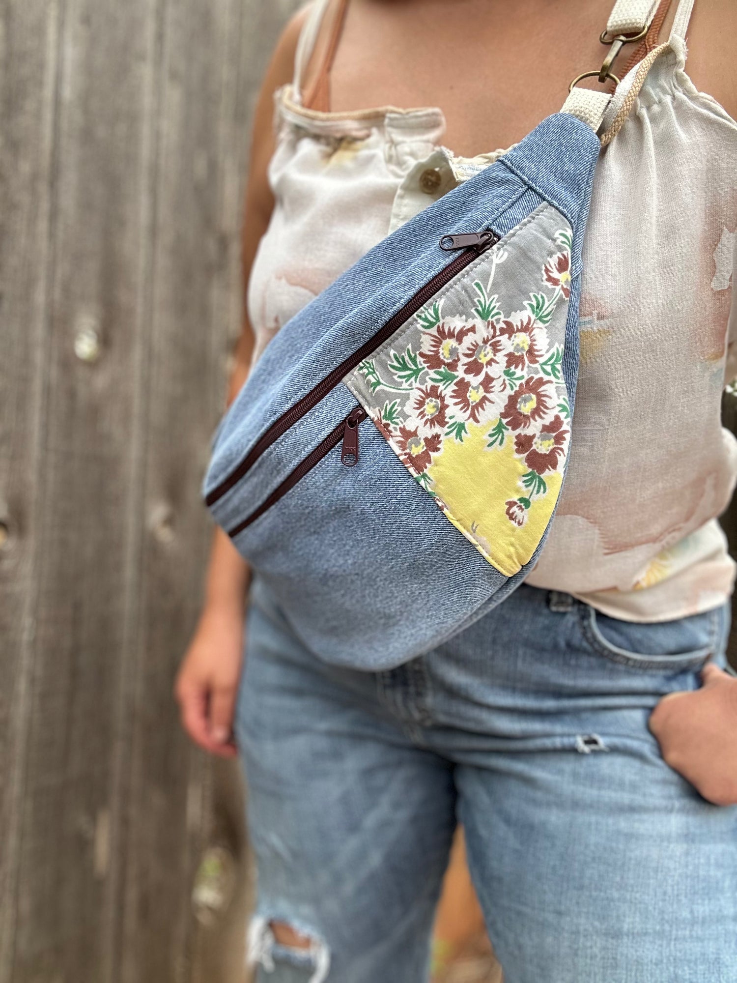 Person wearing a denim crossbody bag with floral pattern over a wooden fence background