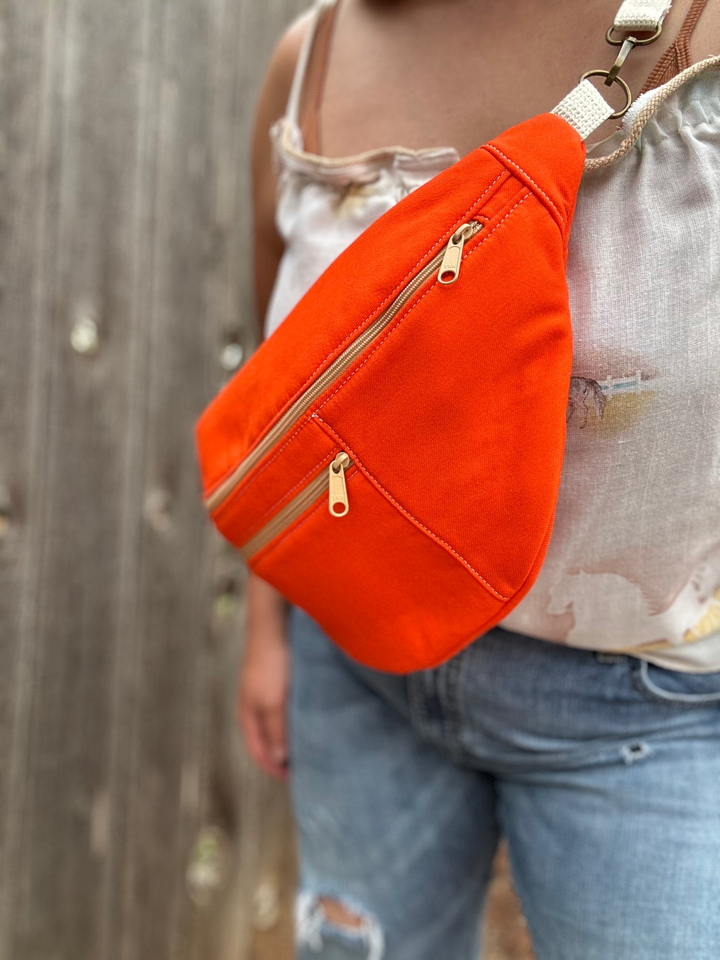 Person wearing an orange fanny pack with beige zippers against a wooden background