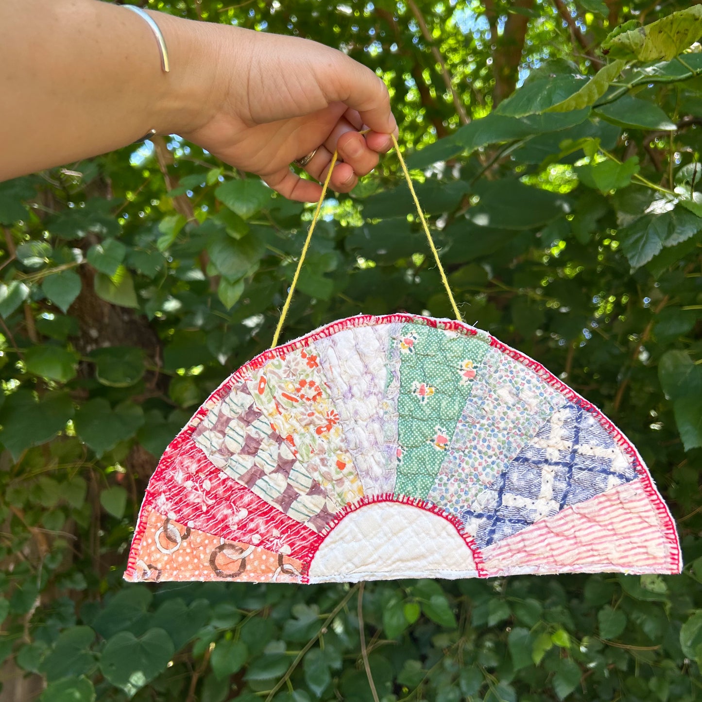 Handmade quilted fan with colorful patterns held against a green leafy background
